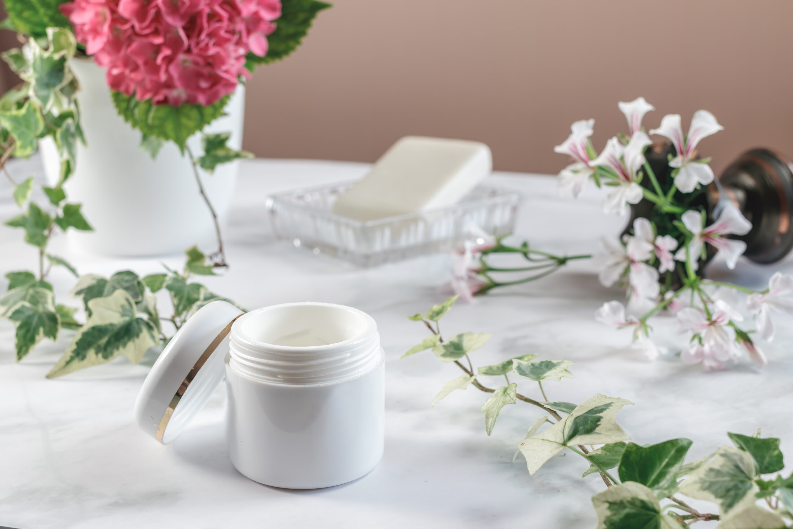 Barattolo di crema naturale su piano in marmo con fiori e sapone — estetica green e minimal.